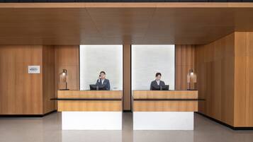 Un área de recepción con dos recepcionistas en mostradores idénticos, paneles de madera y un letrero que indica 'Marriott Bonvoy'.