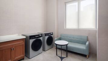 A laundry room with two washing machines, a wooden cabinet, a blue sofa, and a small round table.