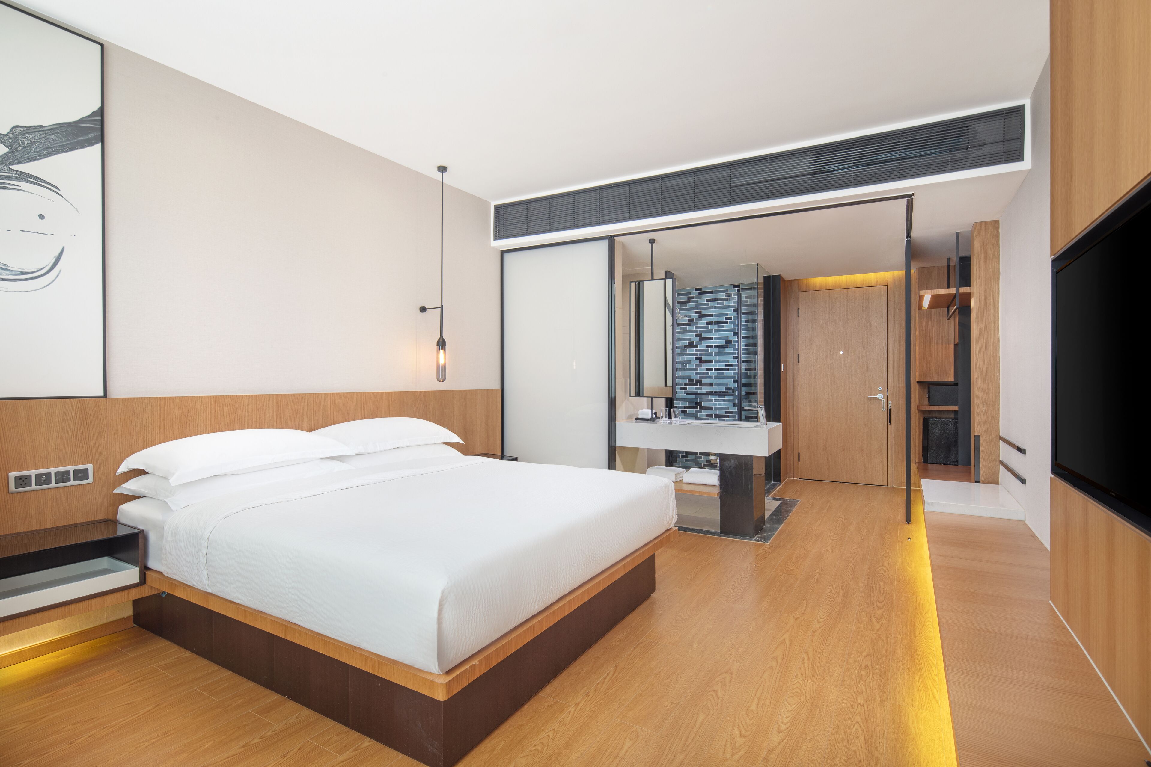 Un dormitorio moderno con una cama grande, mesitas de noche empotradas, un vestidor y un baño con un lavamanos y espejo modernos.