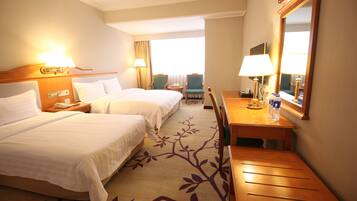A hotel room with two beds, a desk, a chair, a mirror, and a window with curtains.