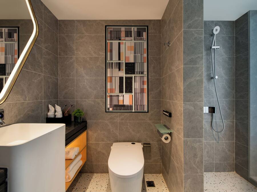 A modern bathroom with a large white sink, a toilet, a shower, and a mirror with a geometric pattern.