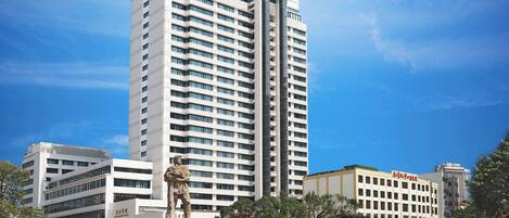 A tall hotel with multiple floors, a statue in front, and a field of red flowers.