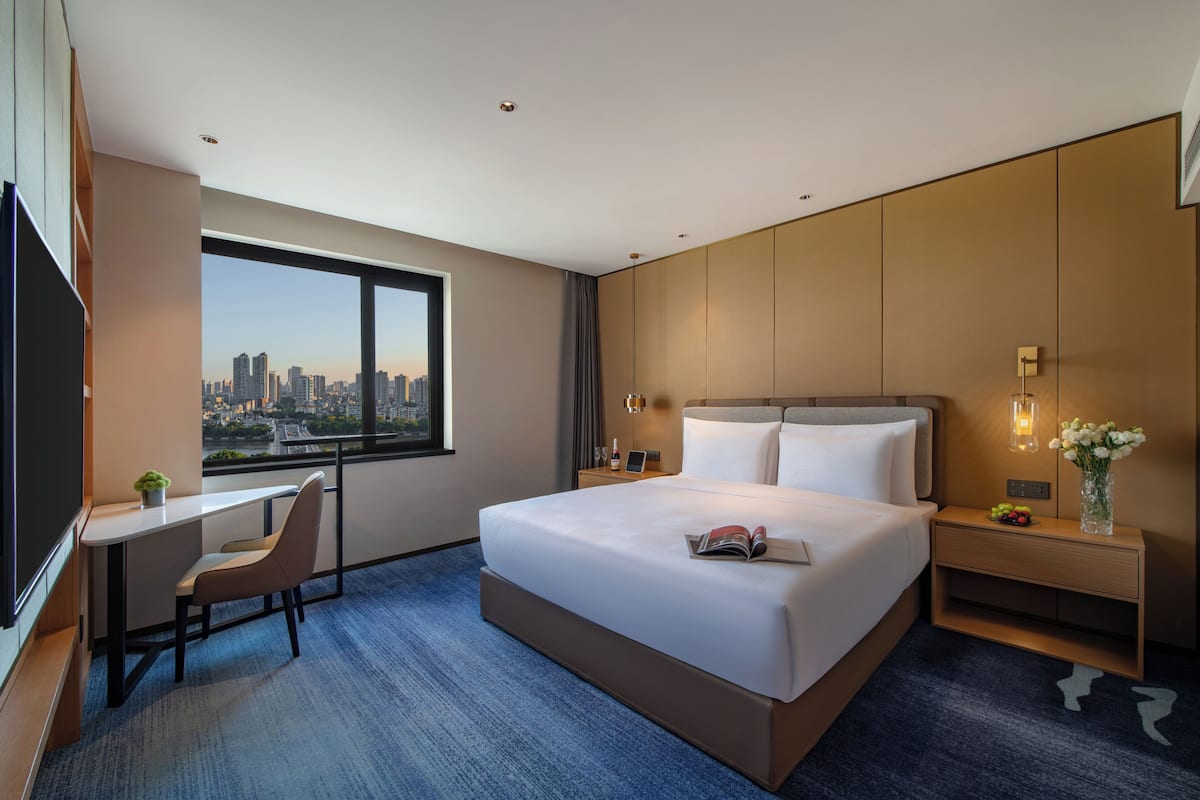 Una habitación de hotel moderna con una cama grande, un escritorio y vistas a un paisaje urbano.