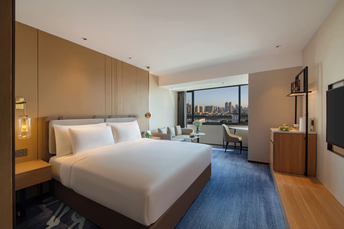 Habitación de hotel moderna con una cama grande, un escritorio, una silla y vistas a un horizonte urbano.