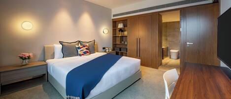 A modern hotel room with a large bed, bedside tables, a desk, and a wardrobe.