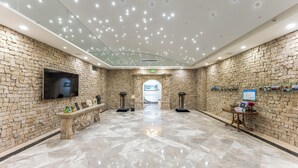 A spacious lobby with a stone wall, a marble floor, a television, a bench, and a reception desk. - AC Embassy Hotel (Beijing)