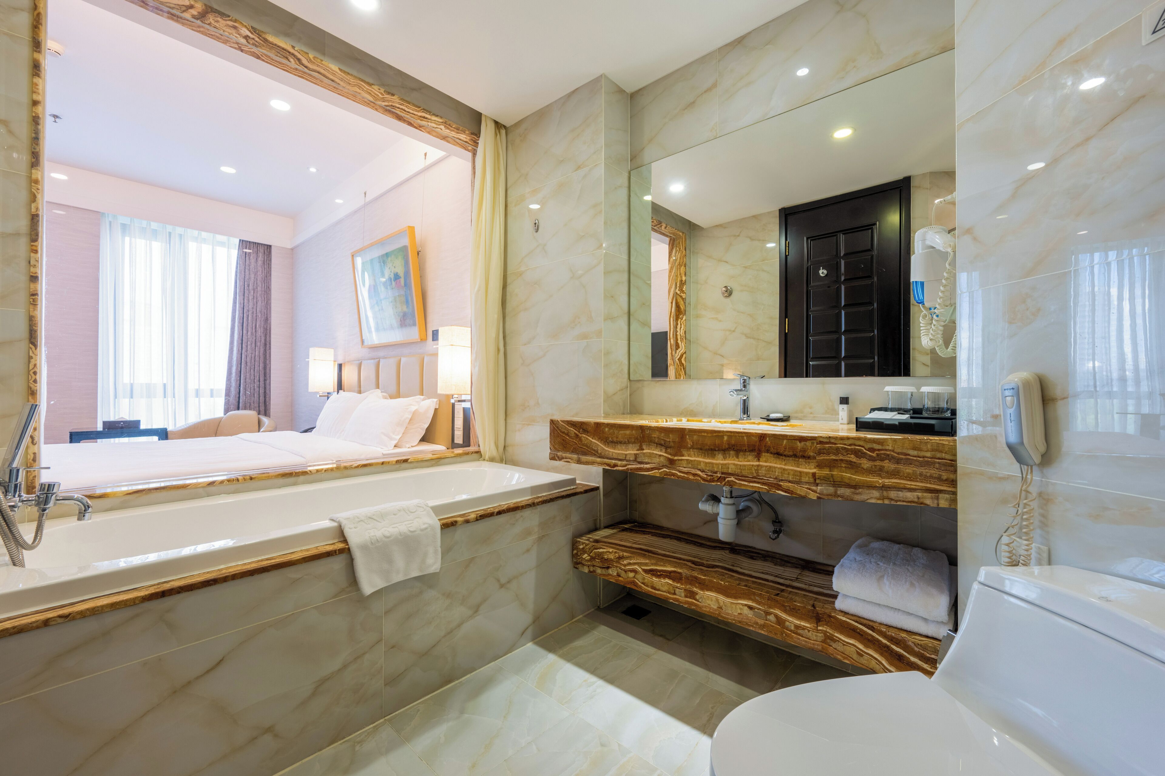 A modern bathroom with a marble vanity, a large mirror, a bathtub, and a toilet.