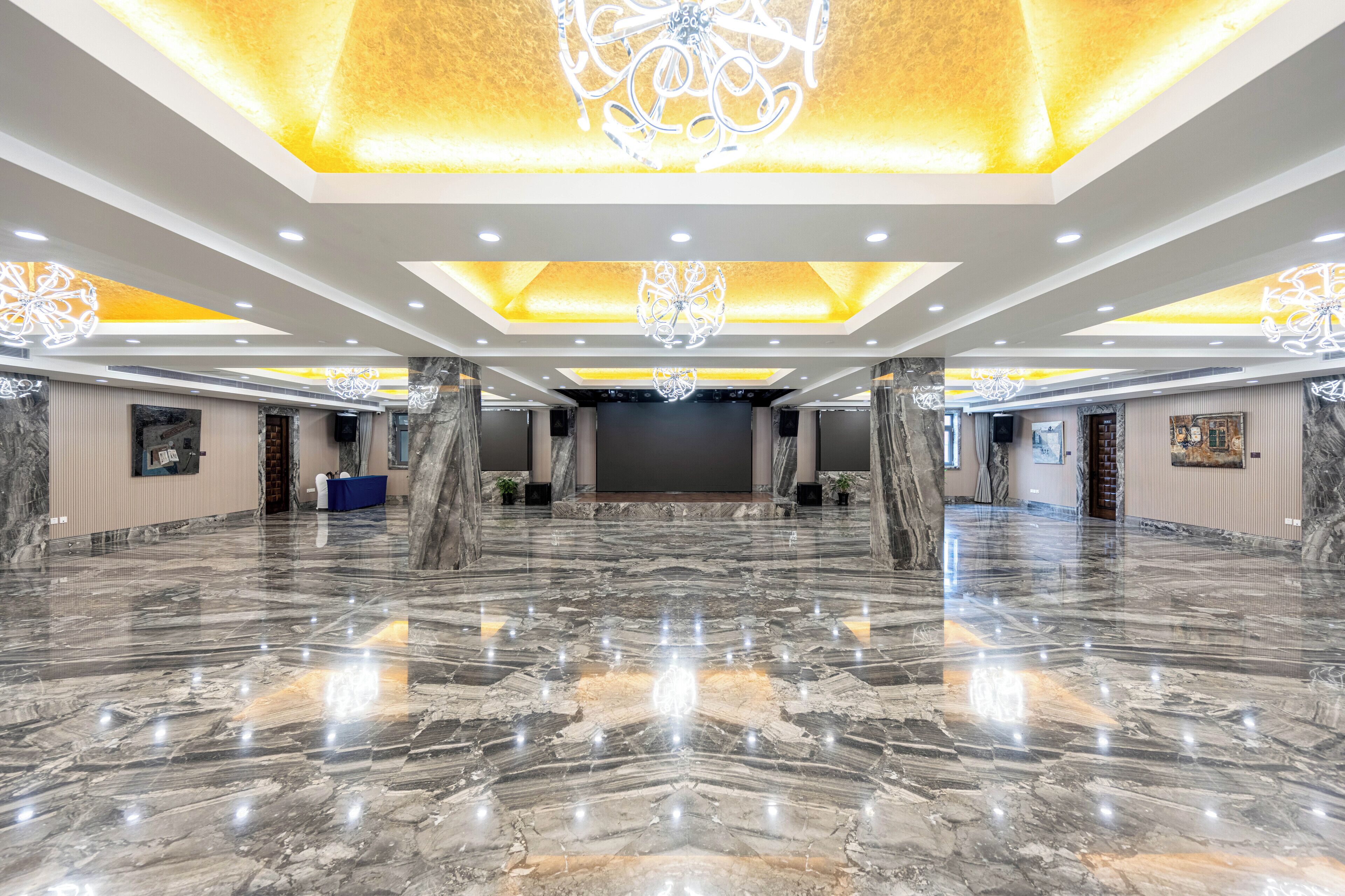 A spacious hall with a polished marble floor, a large screen, and elegant ceiling chandeliers.
