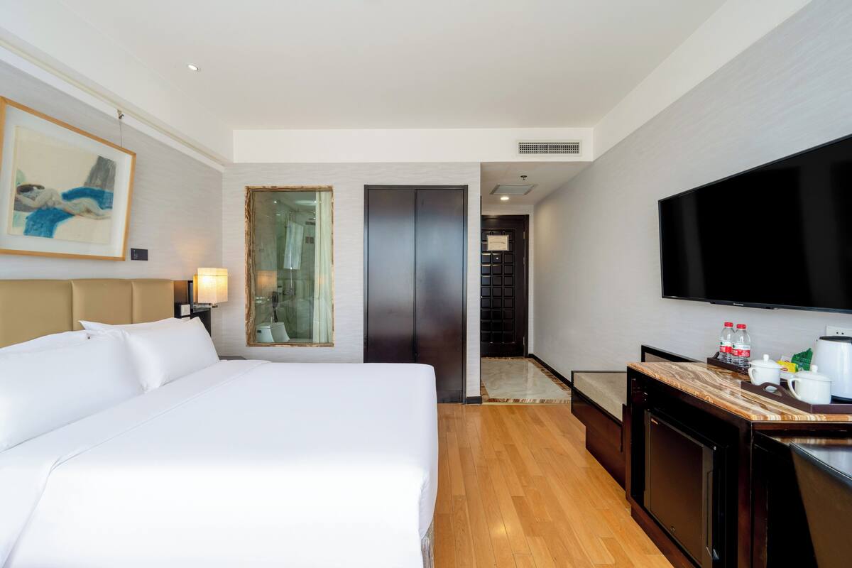 Habitación de hotel con una cama grande, televisión de pantalla plana, piso de madera, escritorio con cafetera y un cuadro en la pared.