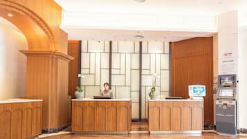 A reception area with wooden reception desks, a receptionist, a digital kiosk, and a tiled floor.