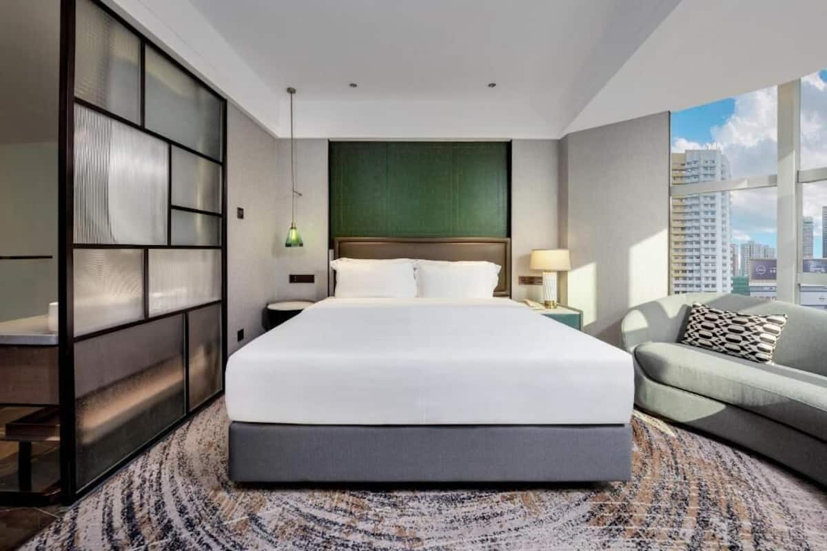 Habitación de hotel moderna con una cama grande, un sofá, vistas de la ciudad y una pared verde decorativa.