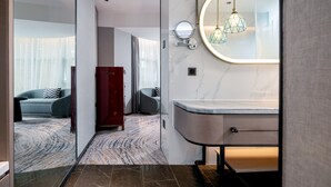 Un baño moderno con encimera de mármol, un espejo redondo y una lámpara colgante de diseño geométrico.