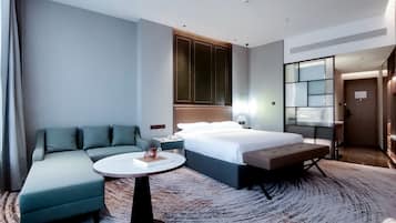 A modern hotel room with a bed, a sofa, a small table, and a large mirror.