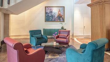 A lobby with a modern design, featuring a seating area with teal and red chairs, a coffee table, and a large painting of a cityscape on the wall.