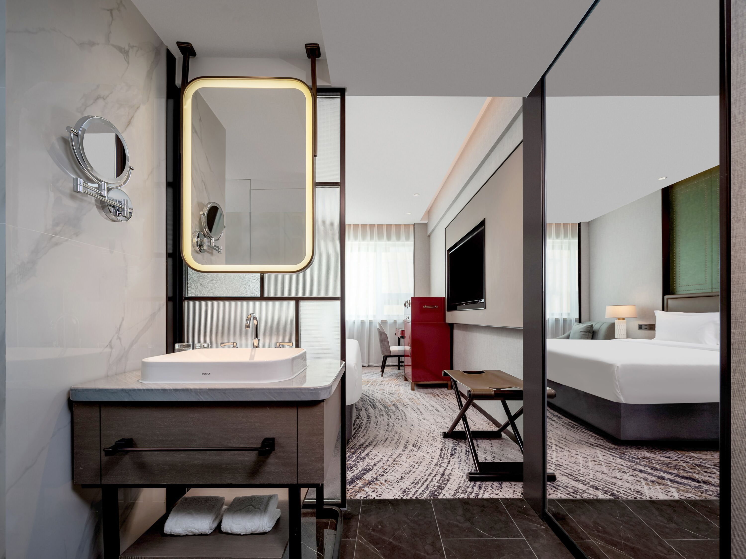 Un baño de hotel moderno con un espejo grande, un lavabo y un mueble rojo.