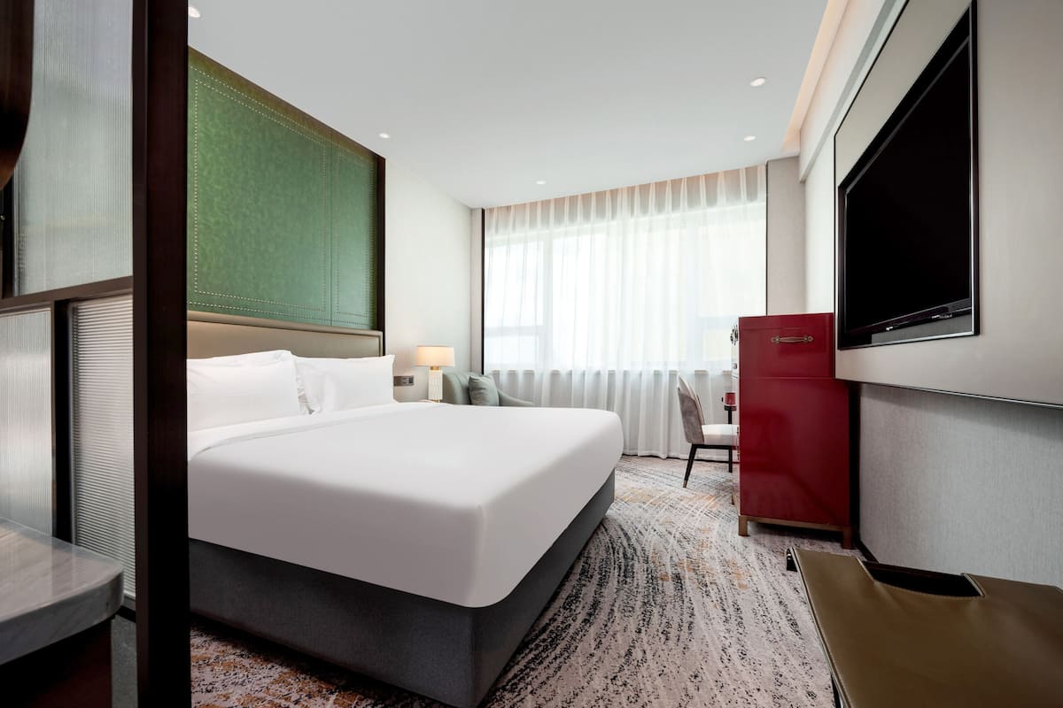 Una habitación de hotel con una cama grande, un escritorio, una silla, un televisor y un minibar rojo.