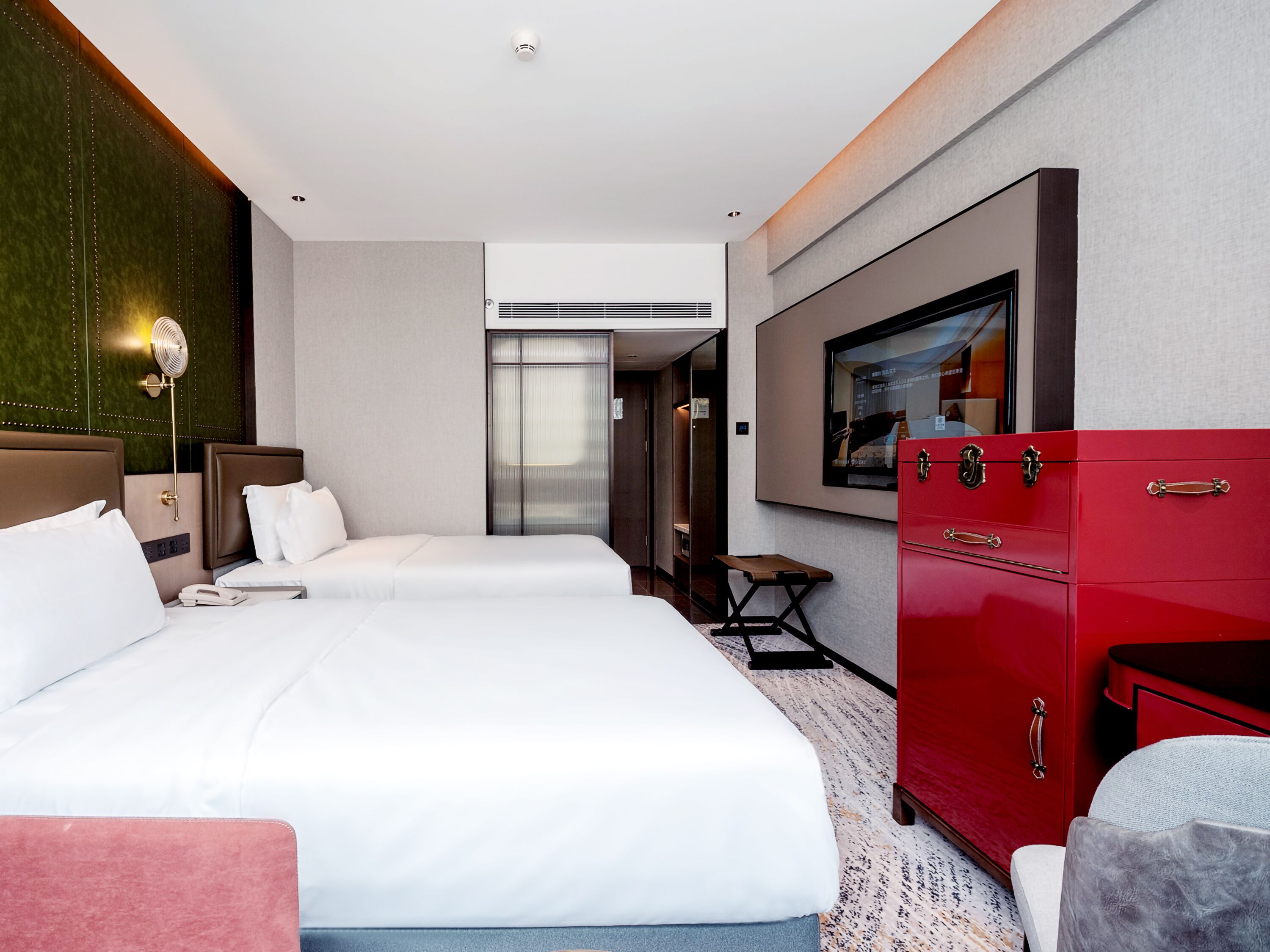 Habitació d'hotel amb dos llits, un armari vermell, una taula petita i un televisor fixat a la paret.