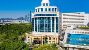 Un edificio moderno con una cúpula y fachada de vidrio, rodeado de vegetación y otros edificios en un paisaje urbano.