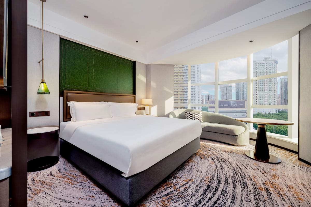 Un hotel moderno con una cama grande, un sofá, una mesa de comedor y vistas de la ciudad a través de amplias ventanas.