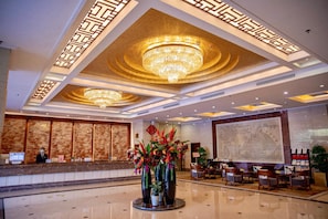 Un hall de hotel con una recepción, una lámpara de araña grande y una zona de estar con sillas.