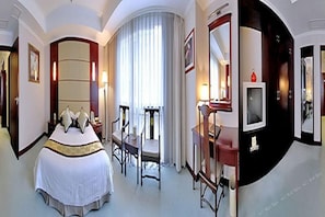 Una habitación de hotel con una cama grande, un escritorio con televisor y una silla.