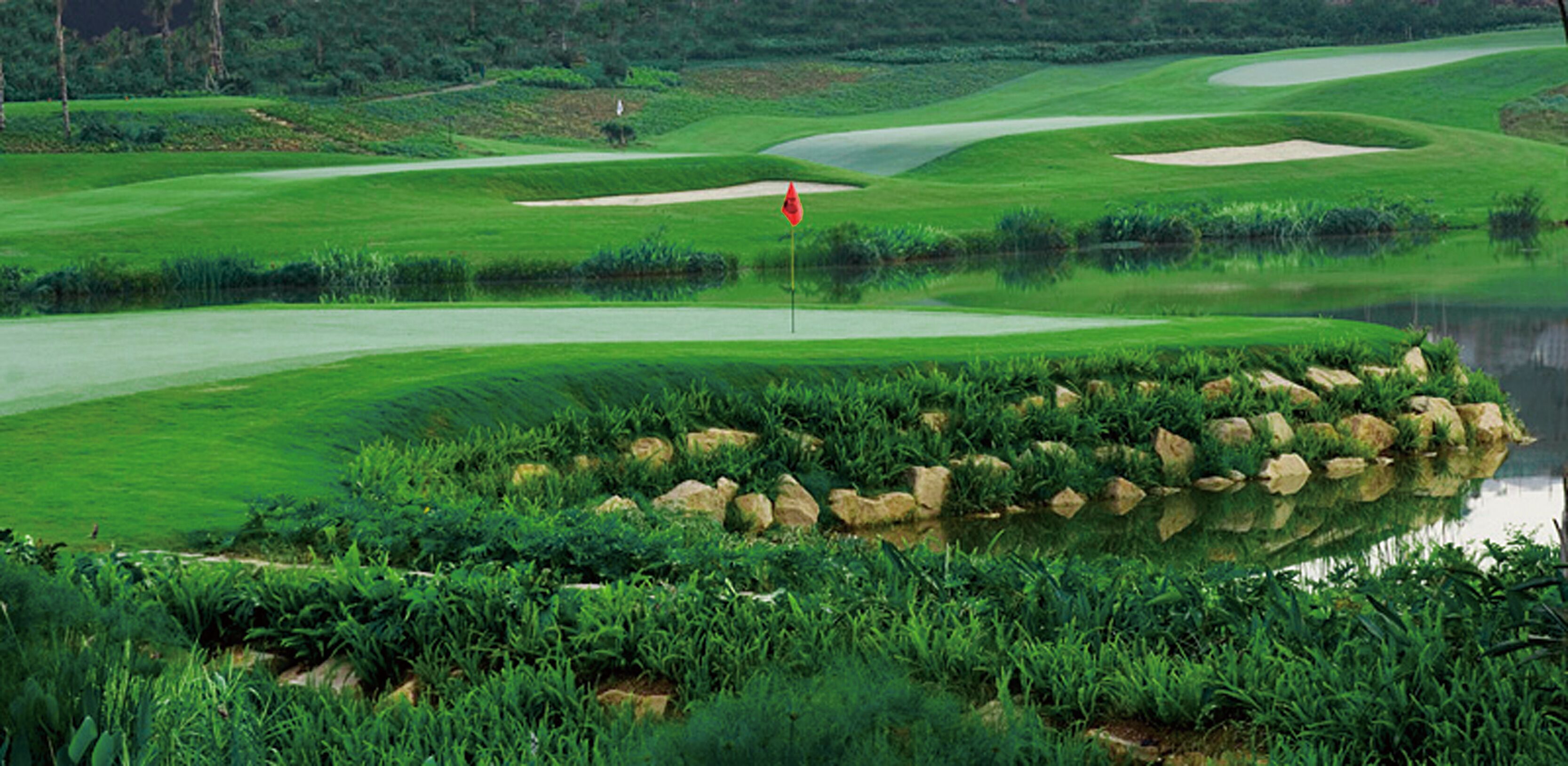 Ein Golfplatz mit Teich, Sandbunkern und einer Fahne auf dem Grün.