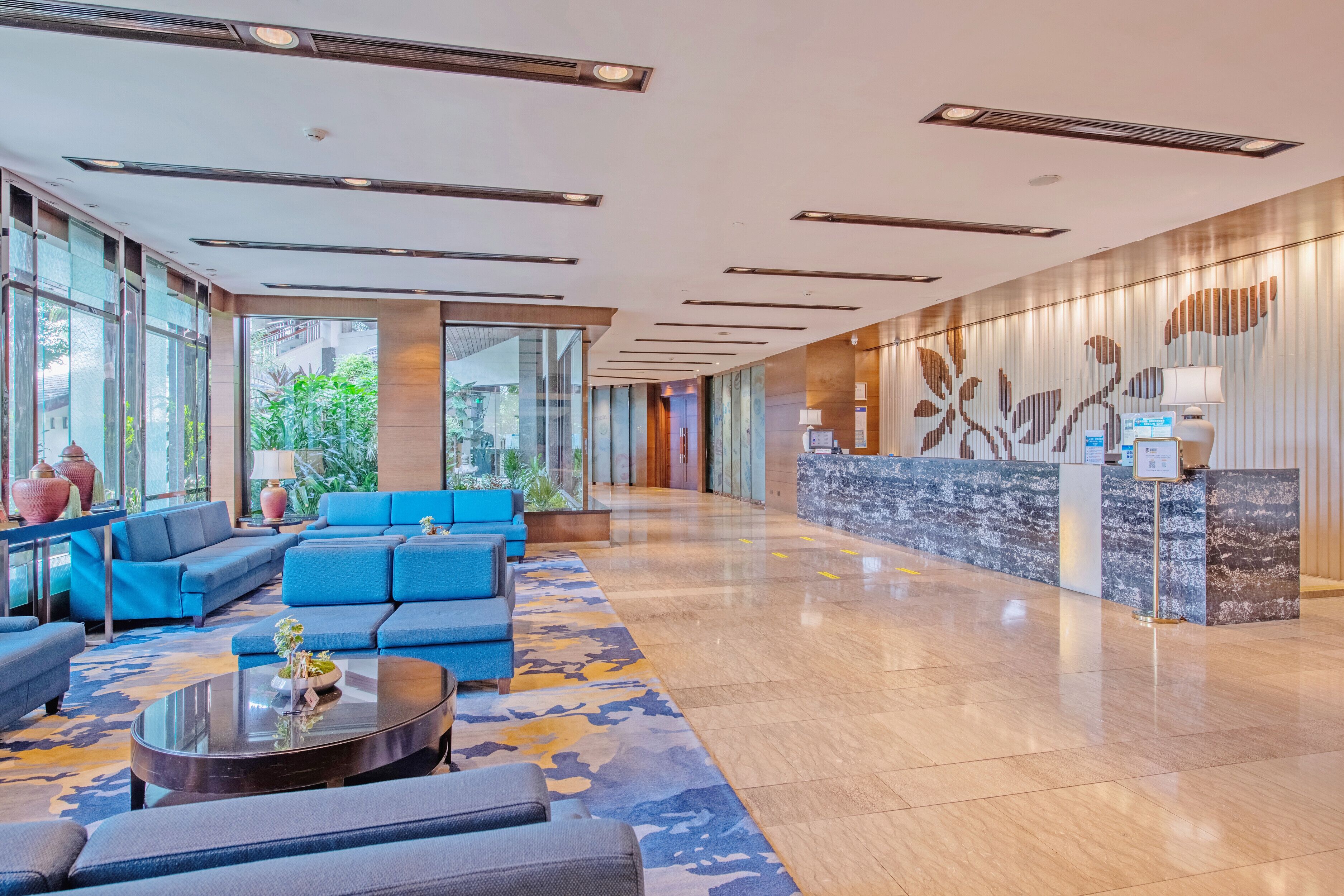 A spacious lobby with blue sofas, a reception desk, and a large window offering a view of greenery.