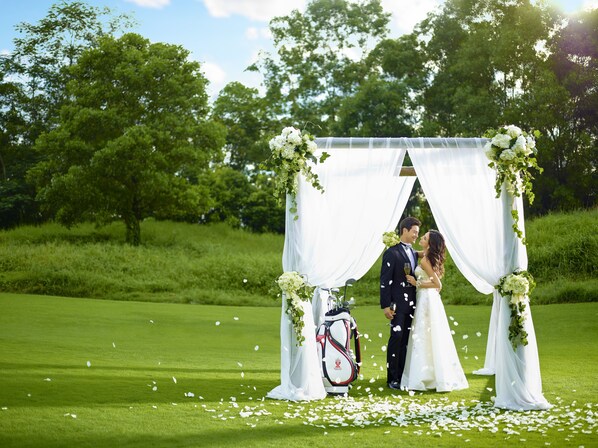 A wedding ceremony with a white canopy and greenery in the background.
