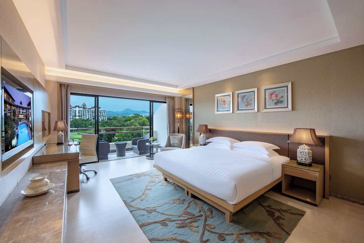 Ein modernes Hotelzimmer mit einem großen Bett, einem Fernseher, einem Schreibtisch mit Stuhl und einem Balkon mit Bergblick.