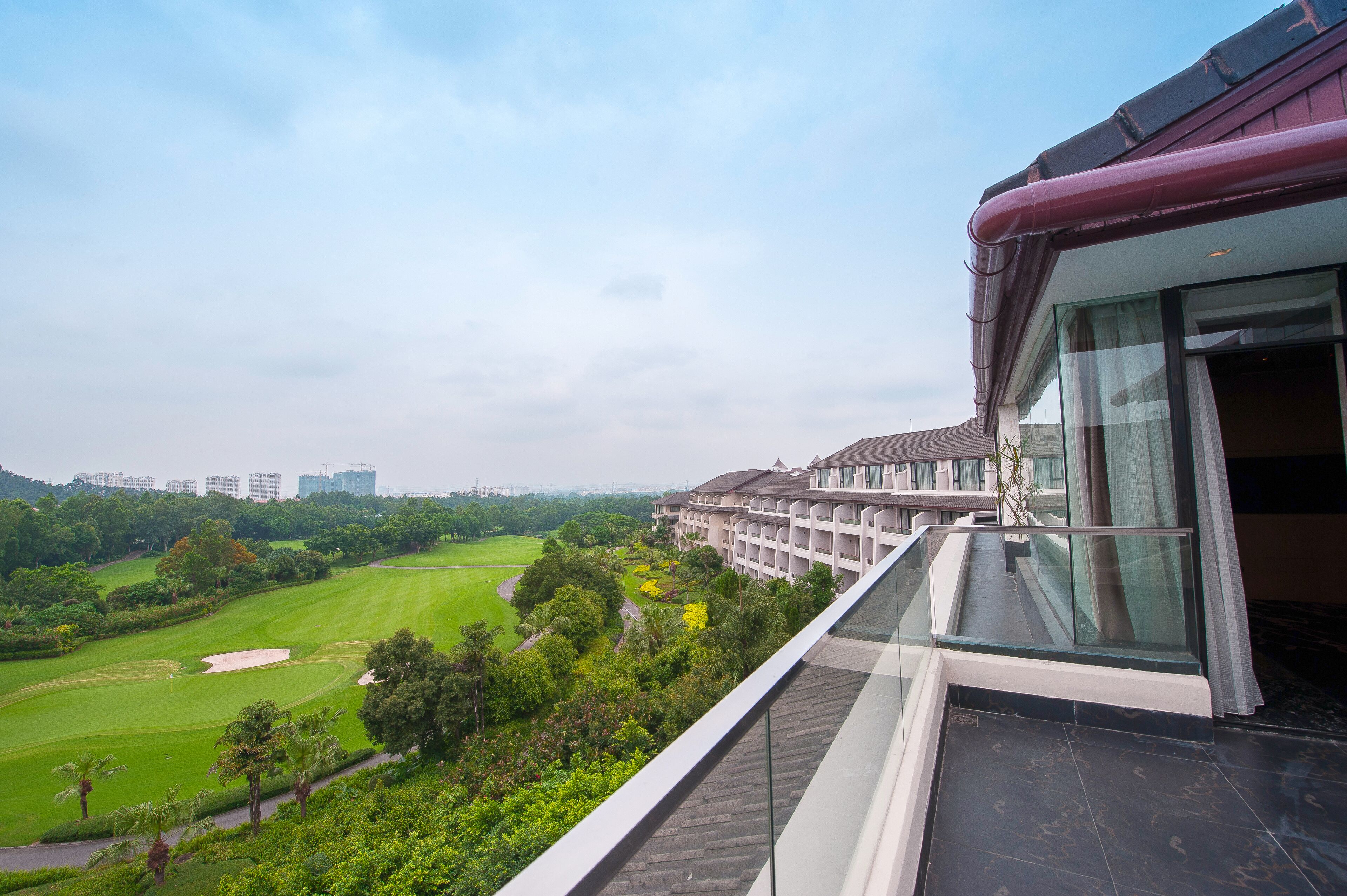 A view of a golf course from a hotel balcony with a modern building in the background.