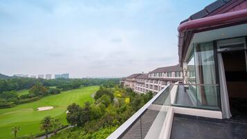 A view of a golf course from a hotel balcony with a modern building in the background.