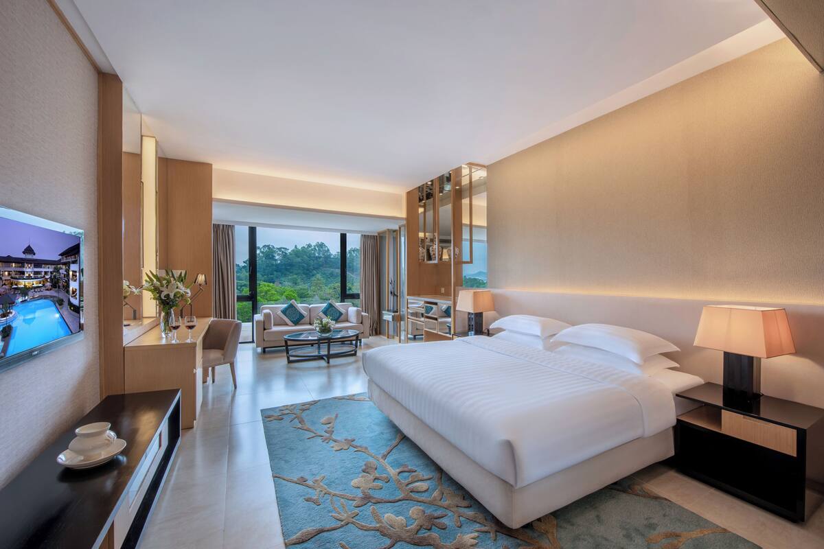 Ein Hotelzimmer mit einem großen Bett, einem Fernseher, einem Schreibtisch mit Computer, einem Couchtisch und einer Couch.