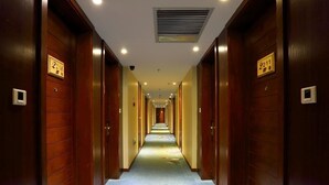 Un couloir d’hôtel avec des portes en bois, des panneaux indiquant le numéro des chambres et un sol recouvert de moquette.