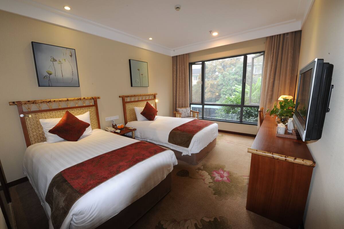 A hotel room with two beds, a television, and a large window with curtains.