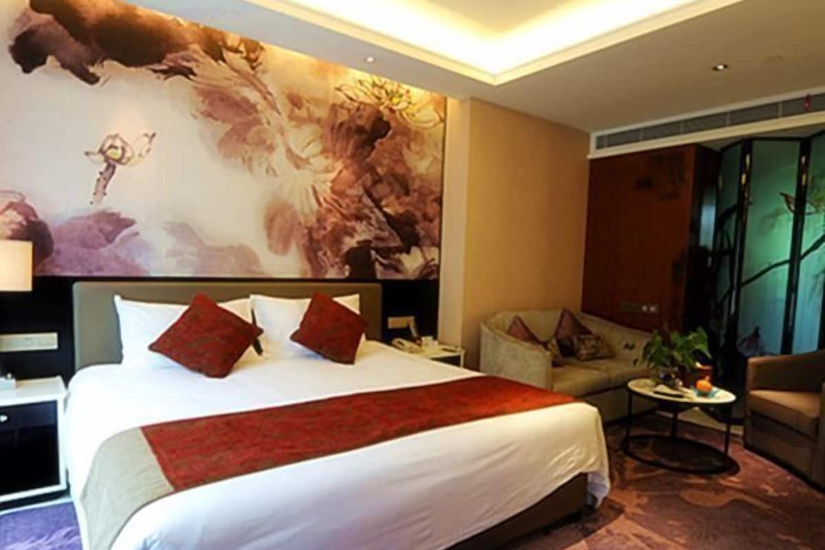 A hotel room with a large bed, a sofa, a small table, and a decorative wall mural.