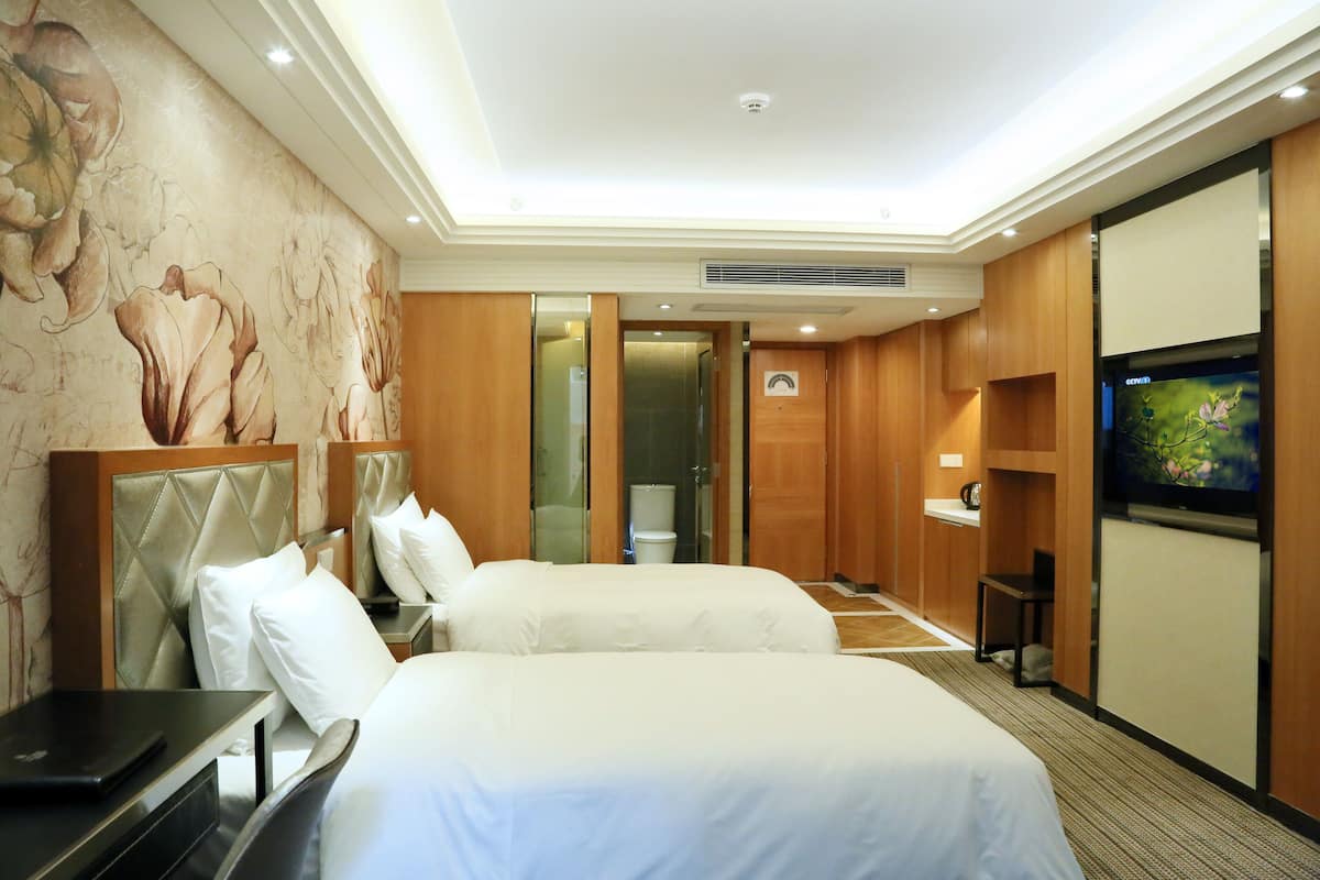 A hotel room with two beds, a television, a desk with a laptop, and a mural on the wall.