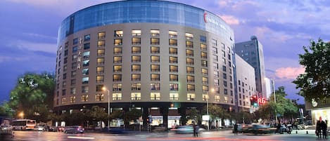 Un hotel con fachada de vidrio curvo, varios pisos y una entrada destacada.