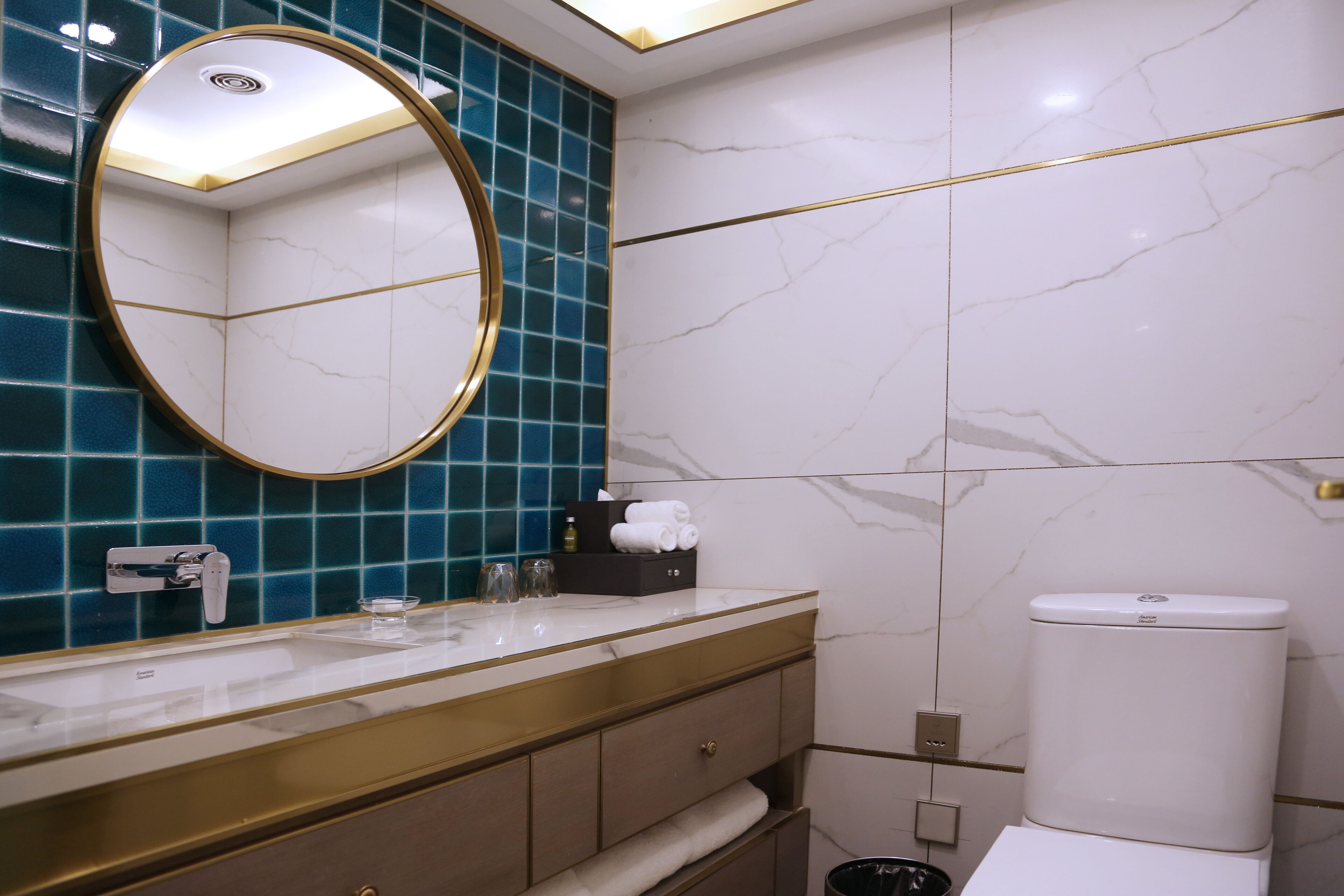 Un baño moderno con tocador de mármol, un espejo redondo y un inodoro.