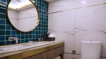 Un baño moderno con tocador de mármol, un espejo redondo y un inodoro.