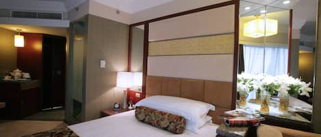 A hotel room with a large bed, a nightstand with a lamp, a mirror, and a floral-patterned pillow.