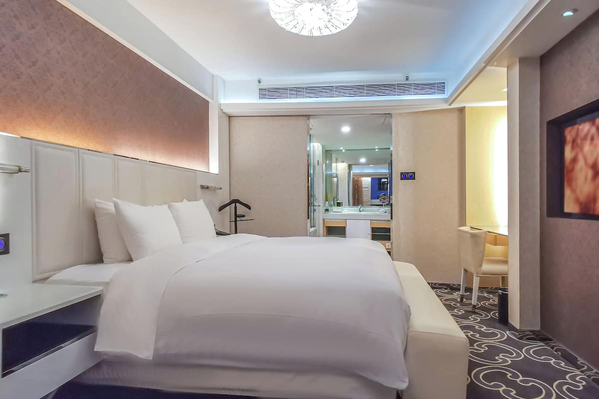 A hotel room with a large bed, a bedside table, a chair, a desk, and a mirror.