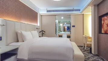Ein Hotelzimmer mit einem großen Bett, einem Nachttisch, einem Sessel, einem Schreibtisch und einem Spiegel.