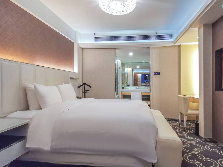 Ein Hotelzimmer mit einem großen Bett, einem Nachttisch, einem Sessel, einem Schreibtisch und einem Spiegel.