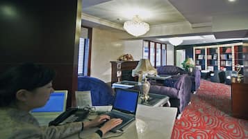 A person working on a laptop in a room with a fireplace, a chandelier, and a bookshelf.