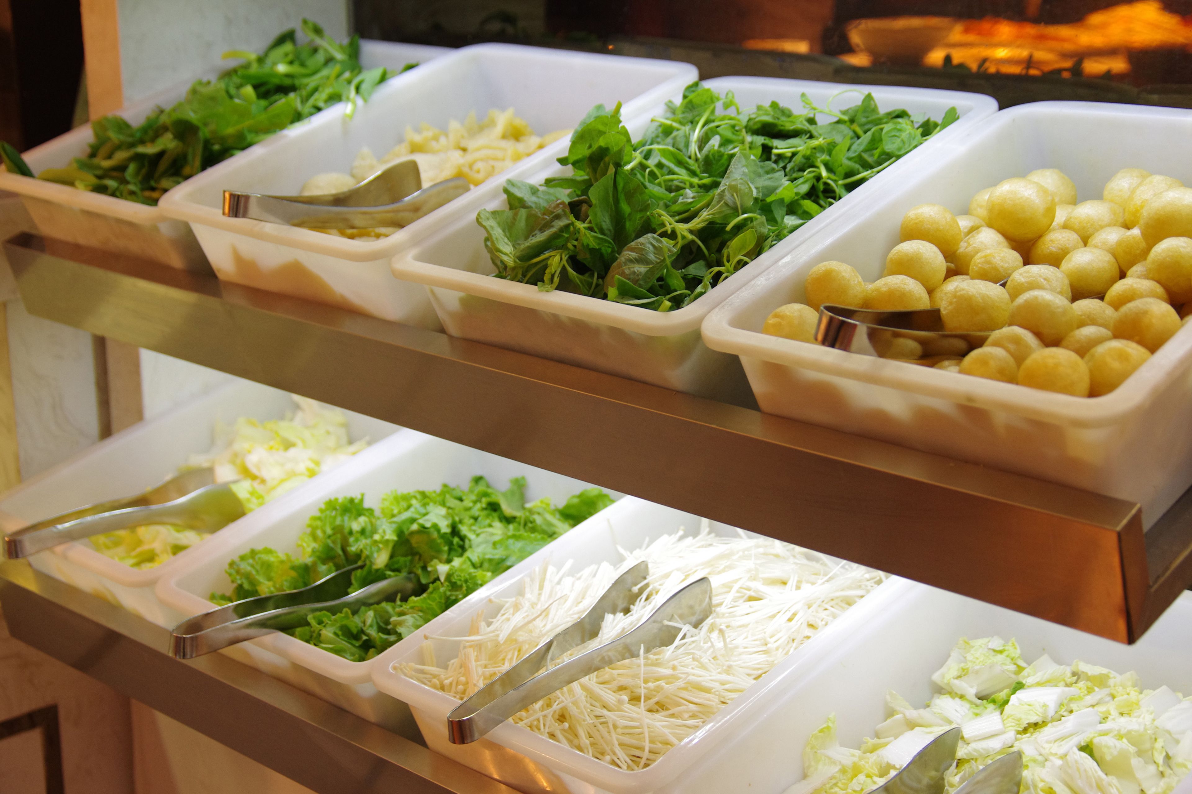 Un bufé con diversas opciones de comida, entre ellas ensaladas, queso y otros platos preparados.