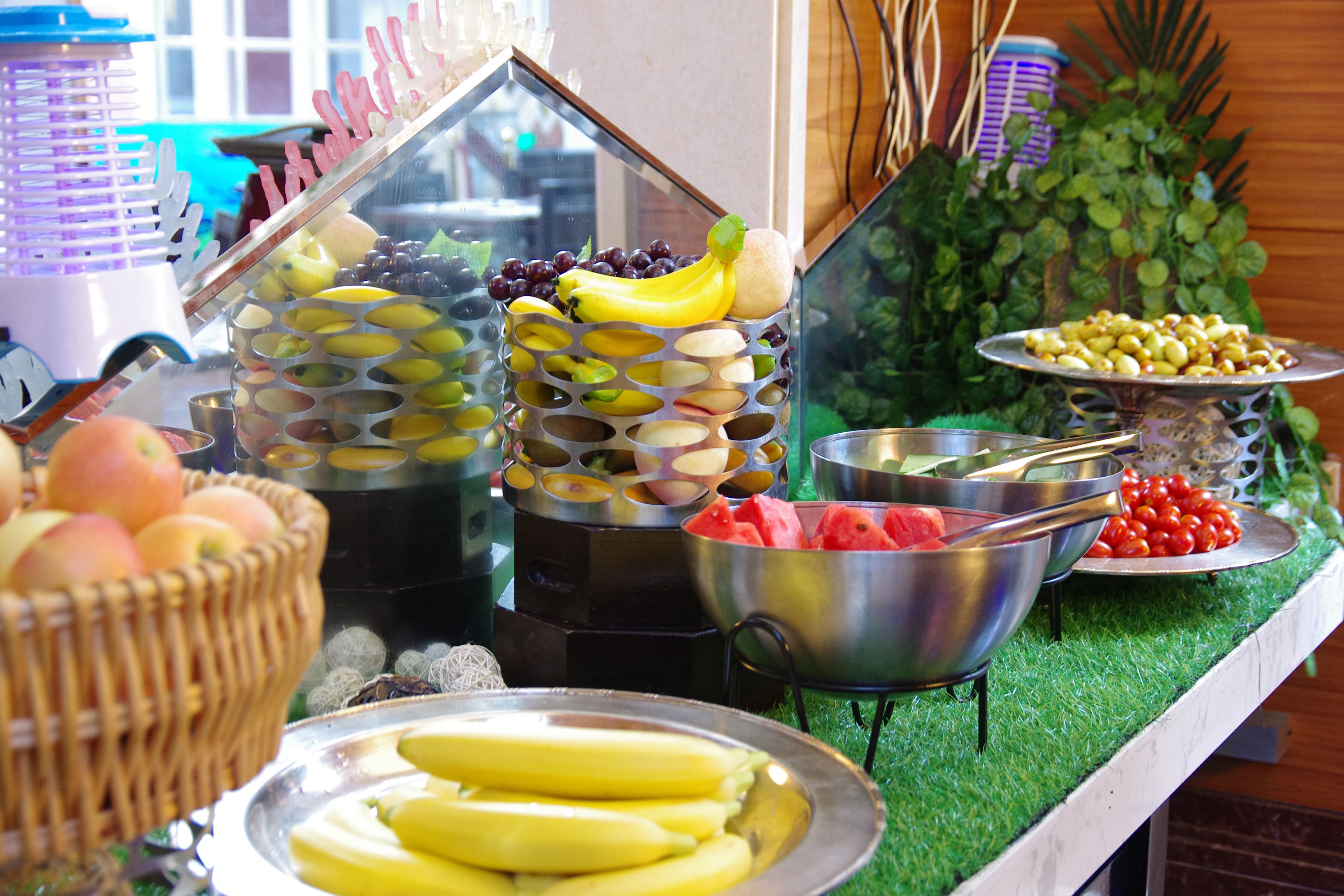 Um buffet com diversas frutas e legumes, incluindo bananas, maçãs e tomates.
