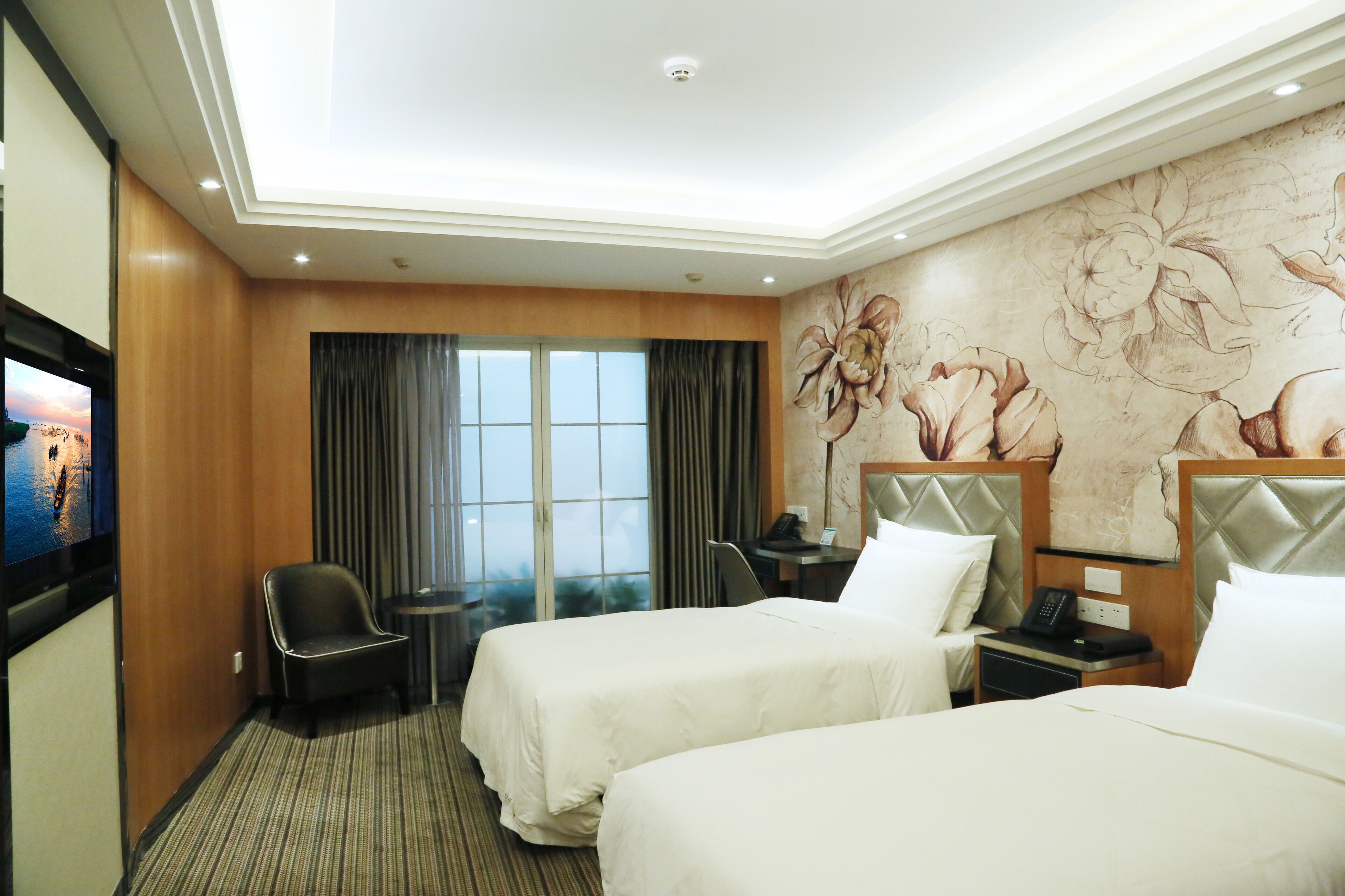 Une chambre d’hôtel avec deux lits, un bureau, une chaise, une télévision et une grande fenêtre avec des rideaux.