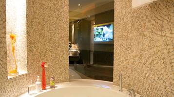 A bathroom with a large bathtub, tiled walls, a towel rack, and a television screen.