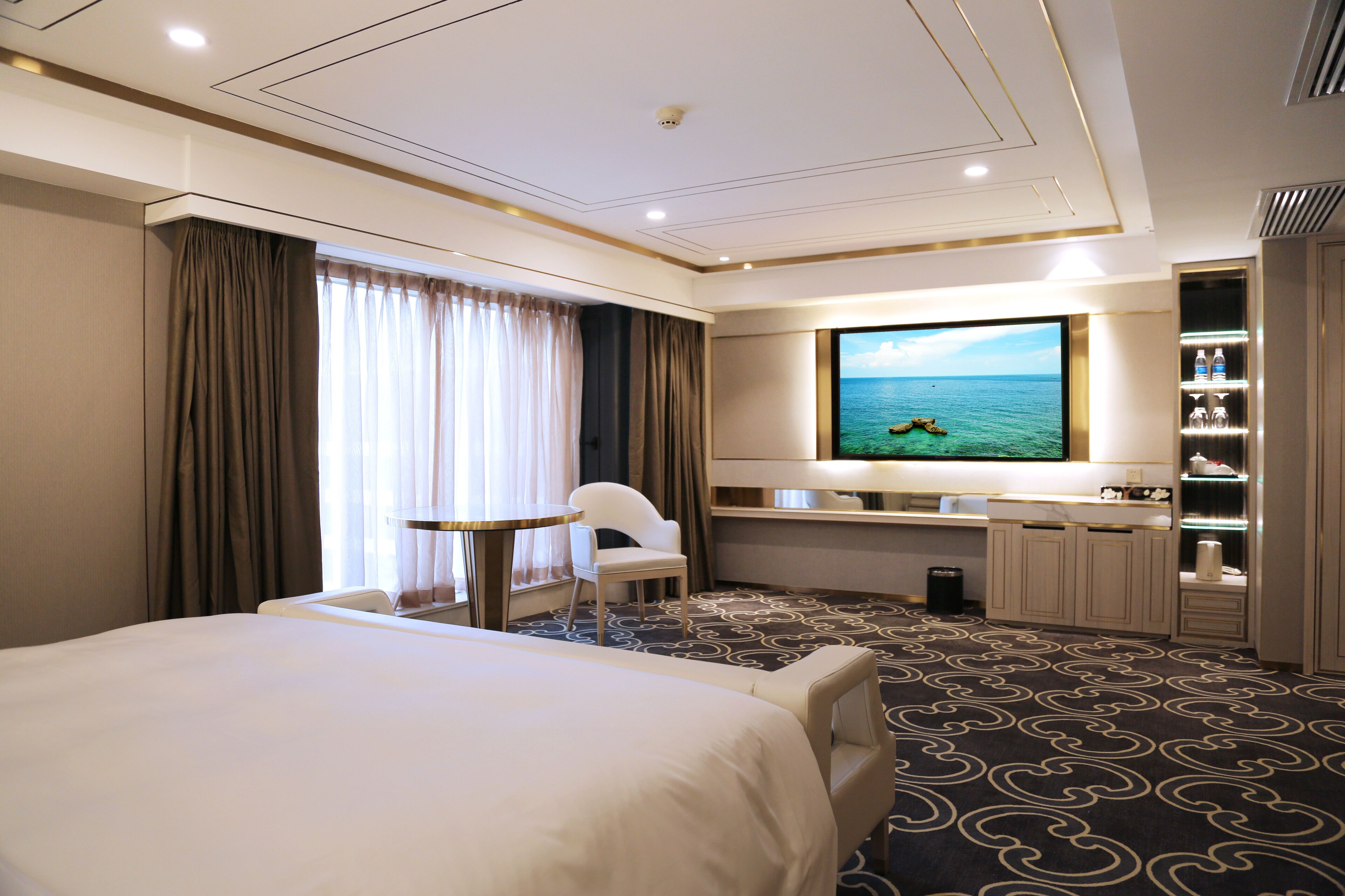 A hotel room with a large bed, a desk with a chair, a television, and a view of the sea.