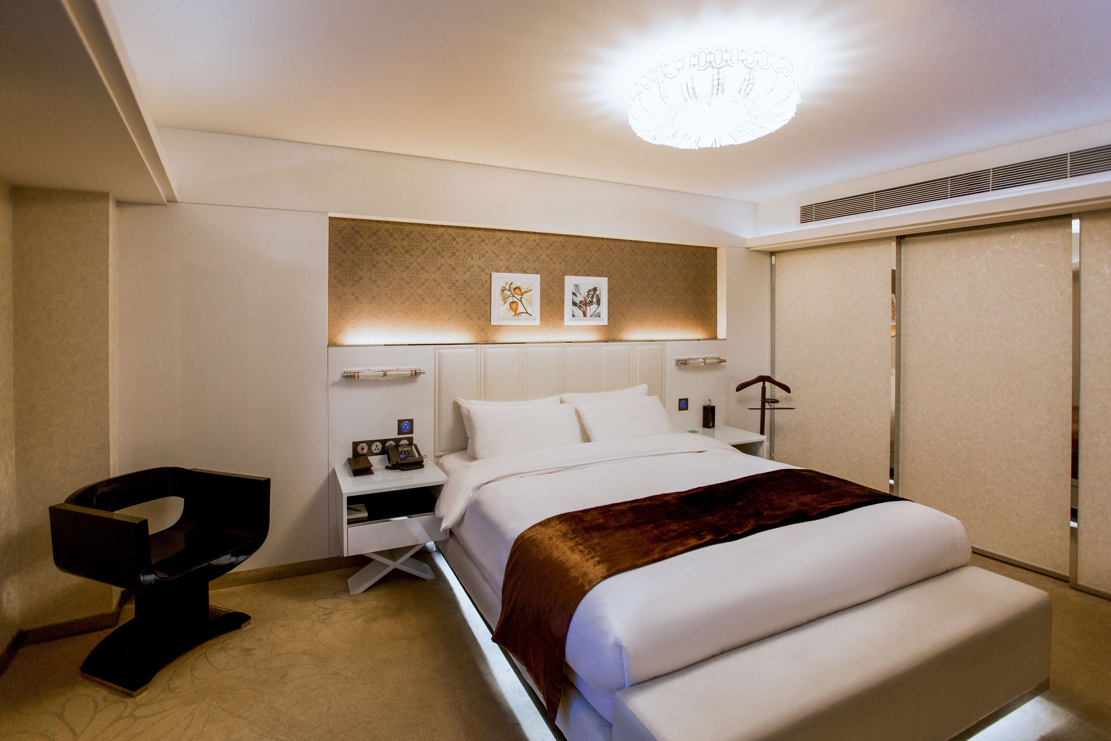 A modern hotel room with a large bed, a bedside table, a chair, and artwork on the wall.